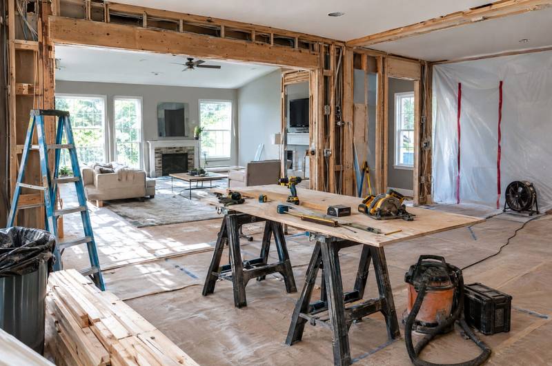 Open living room with wood beams, a stone fireplace, and tall windows